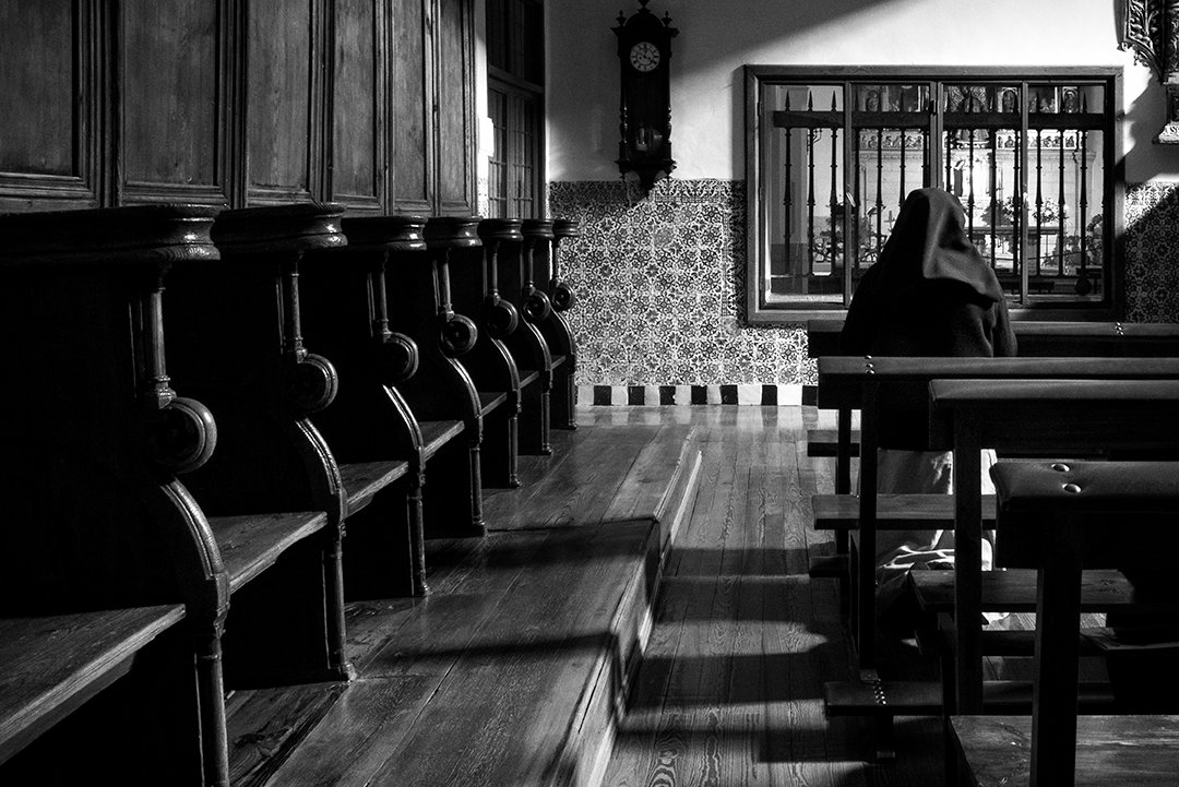 A nun at the far end of a room with wooden choir stalls.